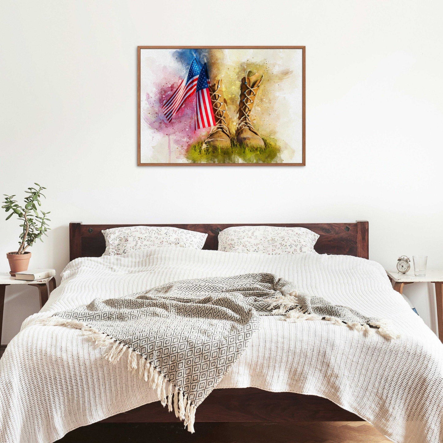 American Flag Wall Art: A framed watercolor print depicting two American flags and military boots in grass, hanging above a bed with white and patterned bedding, flanked by two nightstands with a plant and an alarm clock.