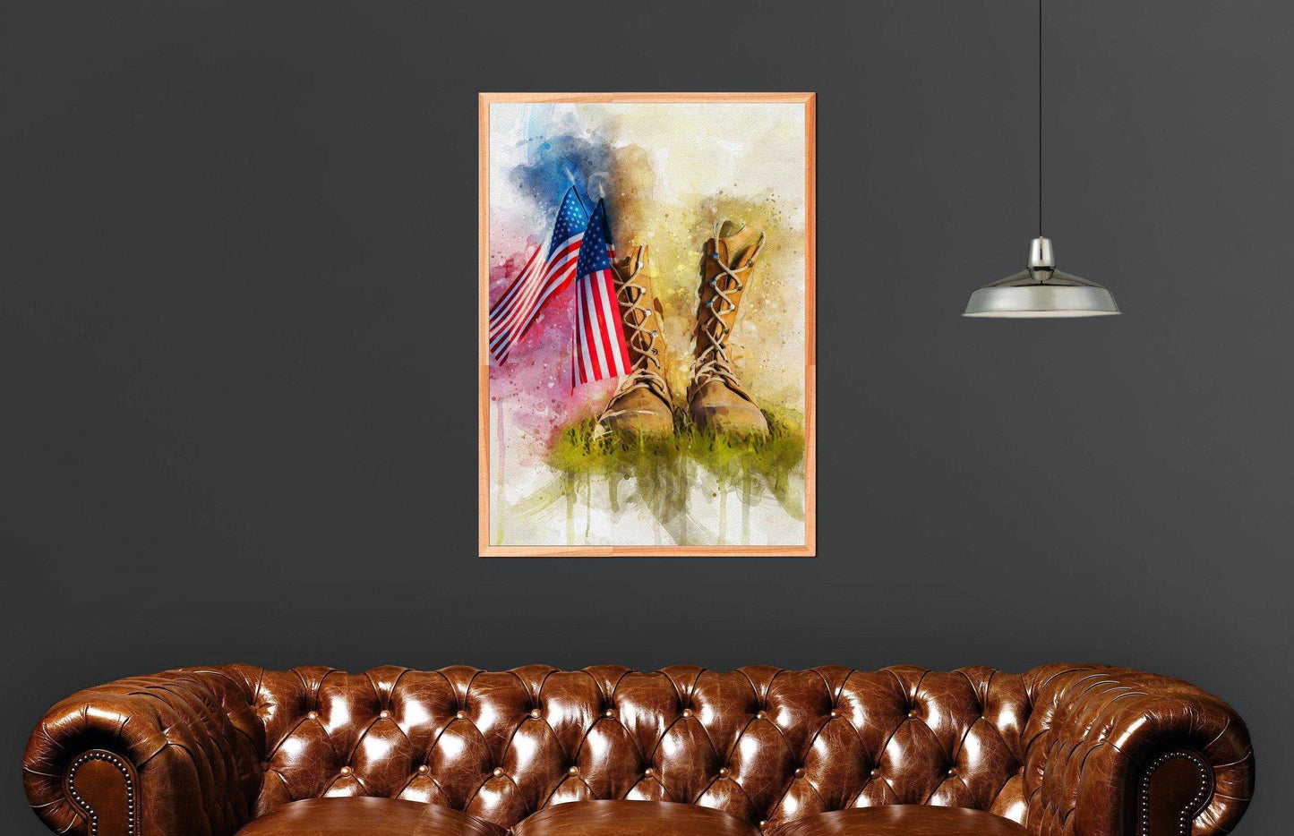 American Flag Wall Art: A framed watercolor print depicting two American flags and military boots in grass, hanging on a dark gray wall above a tufted brown leather sofa with a single industrial-style pendant light overhead.