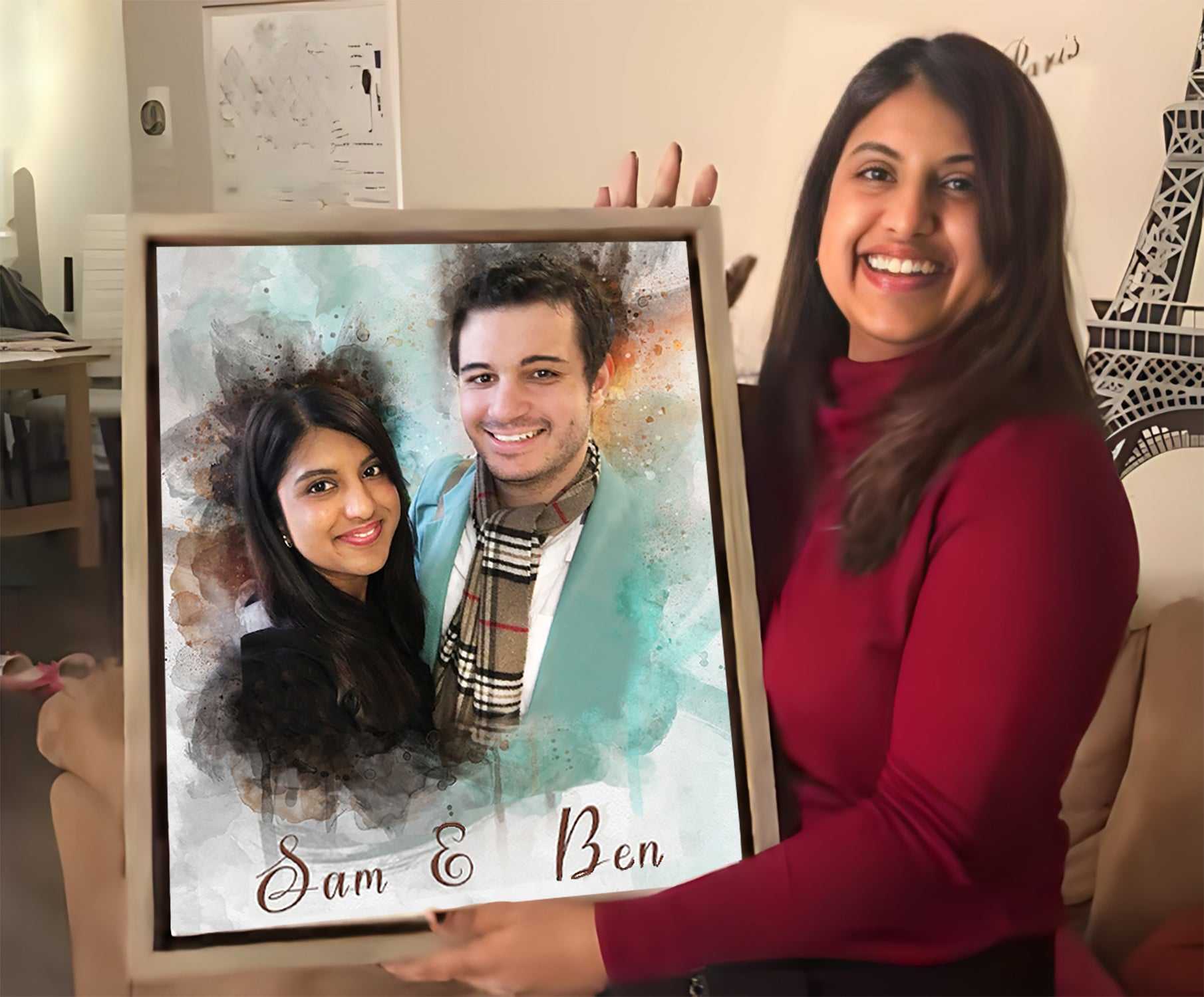 A smiling woman holding a framed custom watercolor portrait by FromPicToArt, depicting a man and a woman. The portrait features the names 'Sam & Ben' and is a thoughtful 7 Year Anniversary Gift.