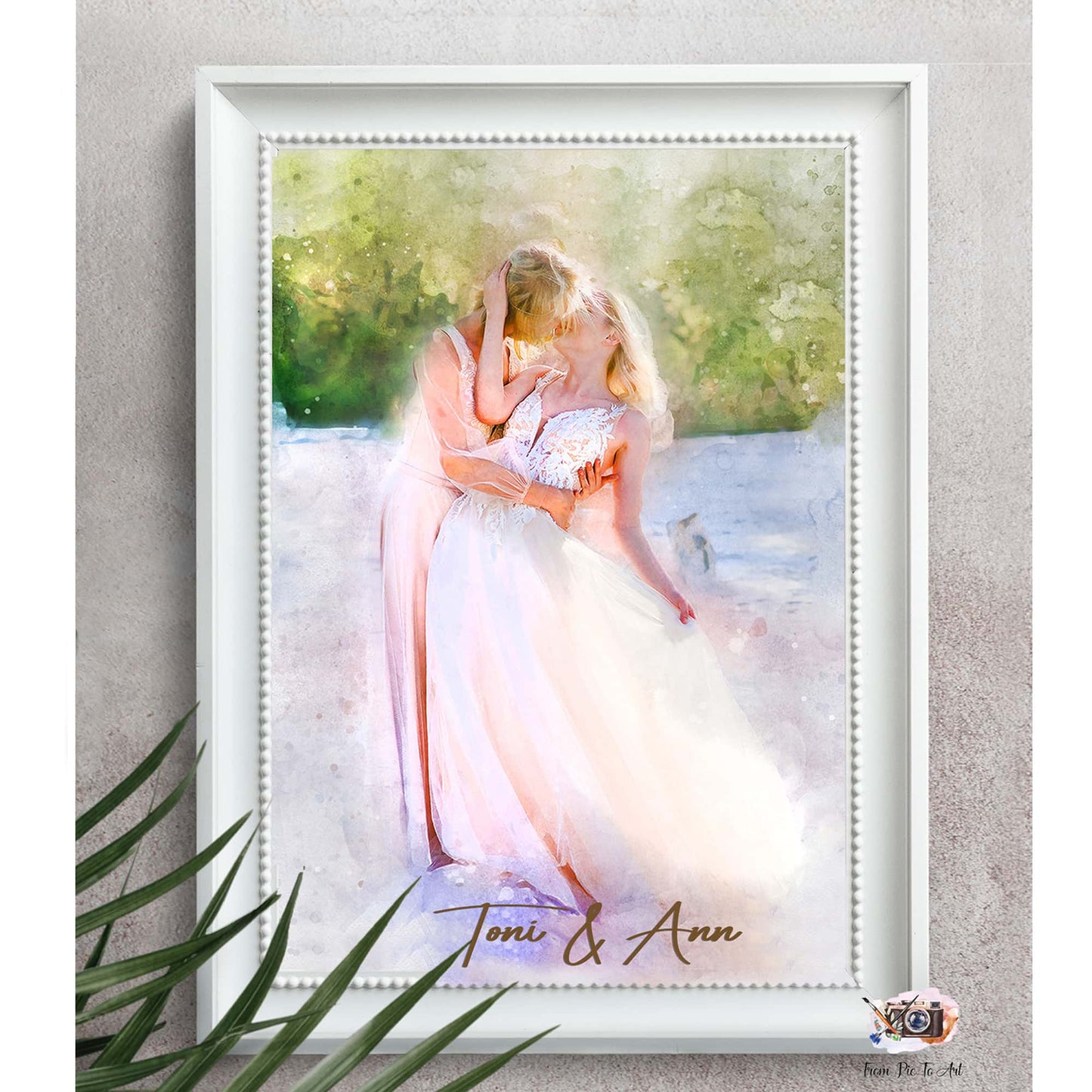 A framed watercolor-style portrait shows two women embracing in what appears to be a wedding setting. One woman wears a flowing white gown, while the other wears a pink dress and kisses her partner's forehead. This romantic artwork is a beautiful example of lesbian gifts.