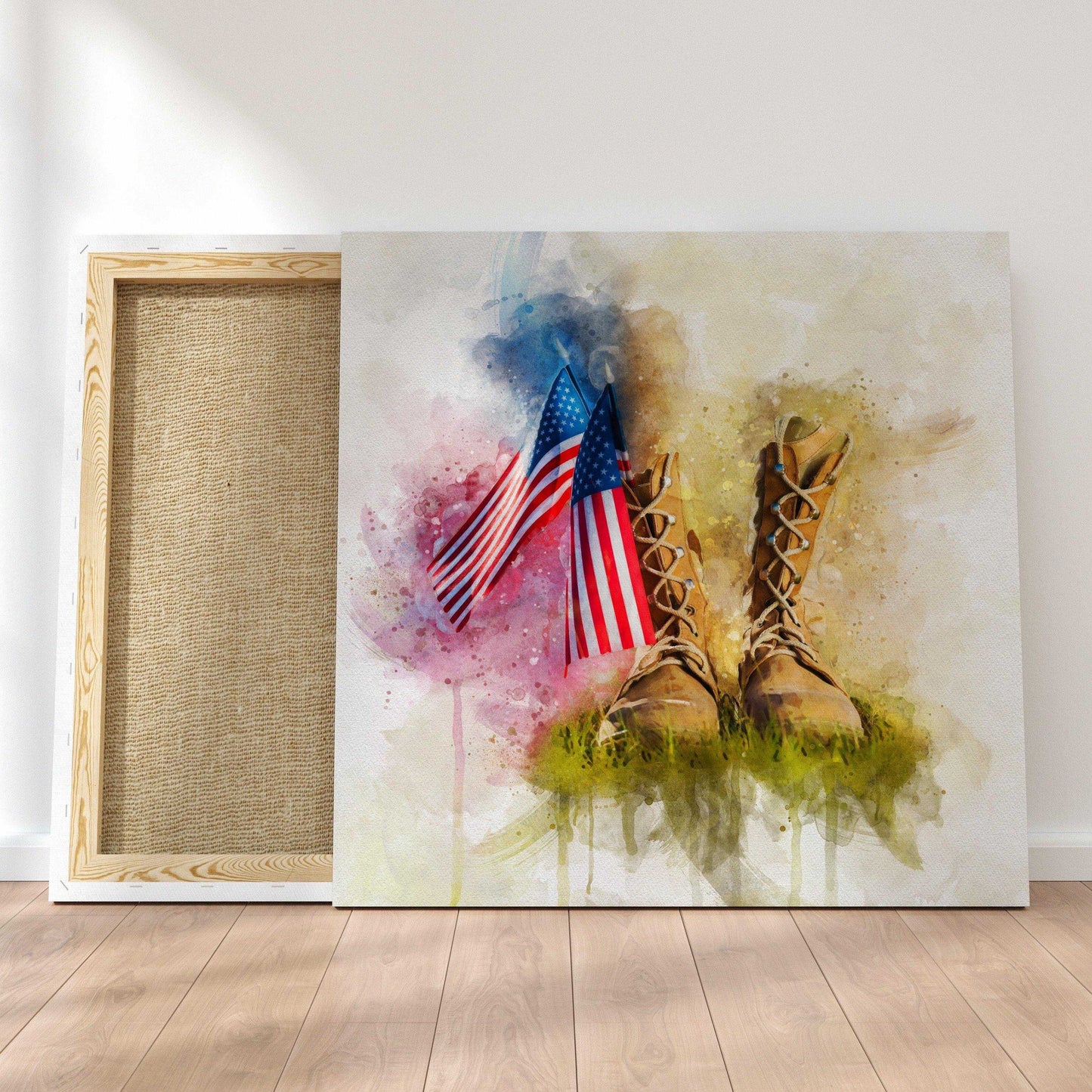 American Flag Wall Art: A canvas print featuring a watercolor image of two American flags and military boots in grass with a colorful splash background, leaning against a white wall next to another canvas showing its stretcher bar frame and back.