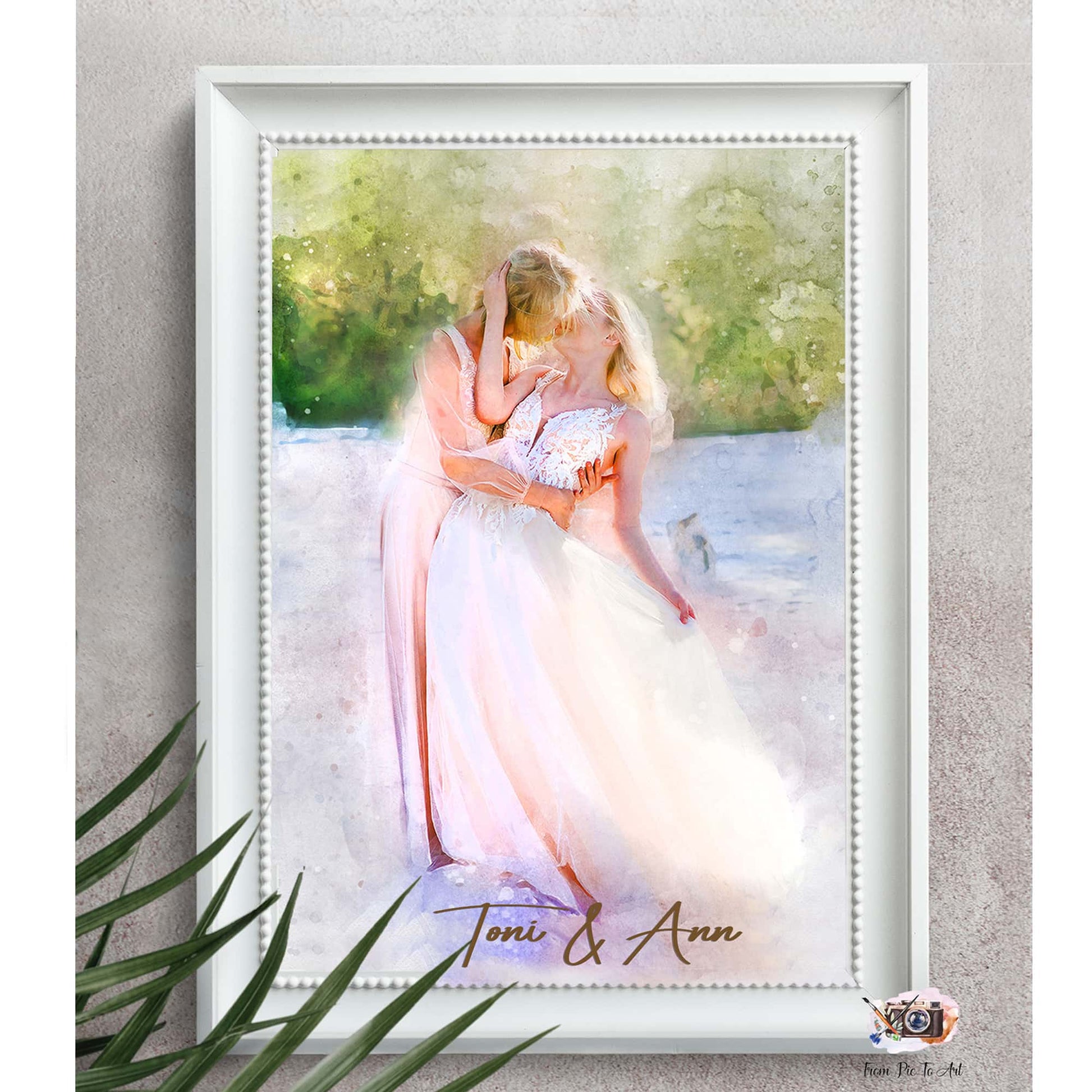 A framed watercolor-style portrait shows two women embracing in what appears to be a wedding setting. One woman wears a flowing white gown, while the other wears a pink dress and kisses her partner's forehead. This romantic artwork is a beautiful example of lesbian gifts.